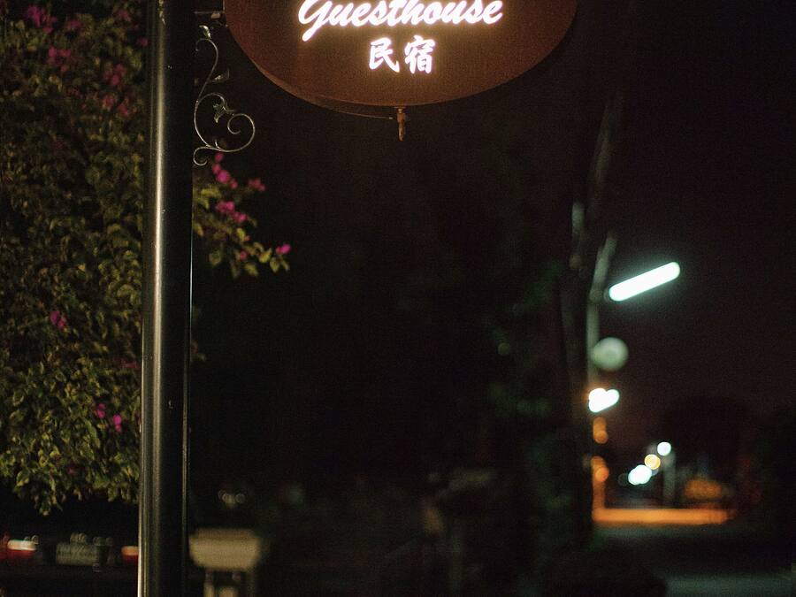 A neon sign for "R&J Guesthouse" in a dark outdoor setting.