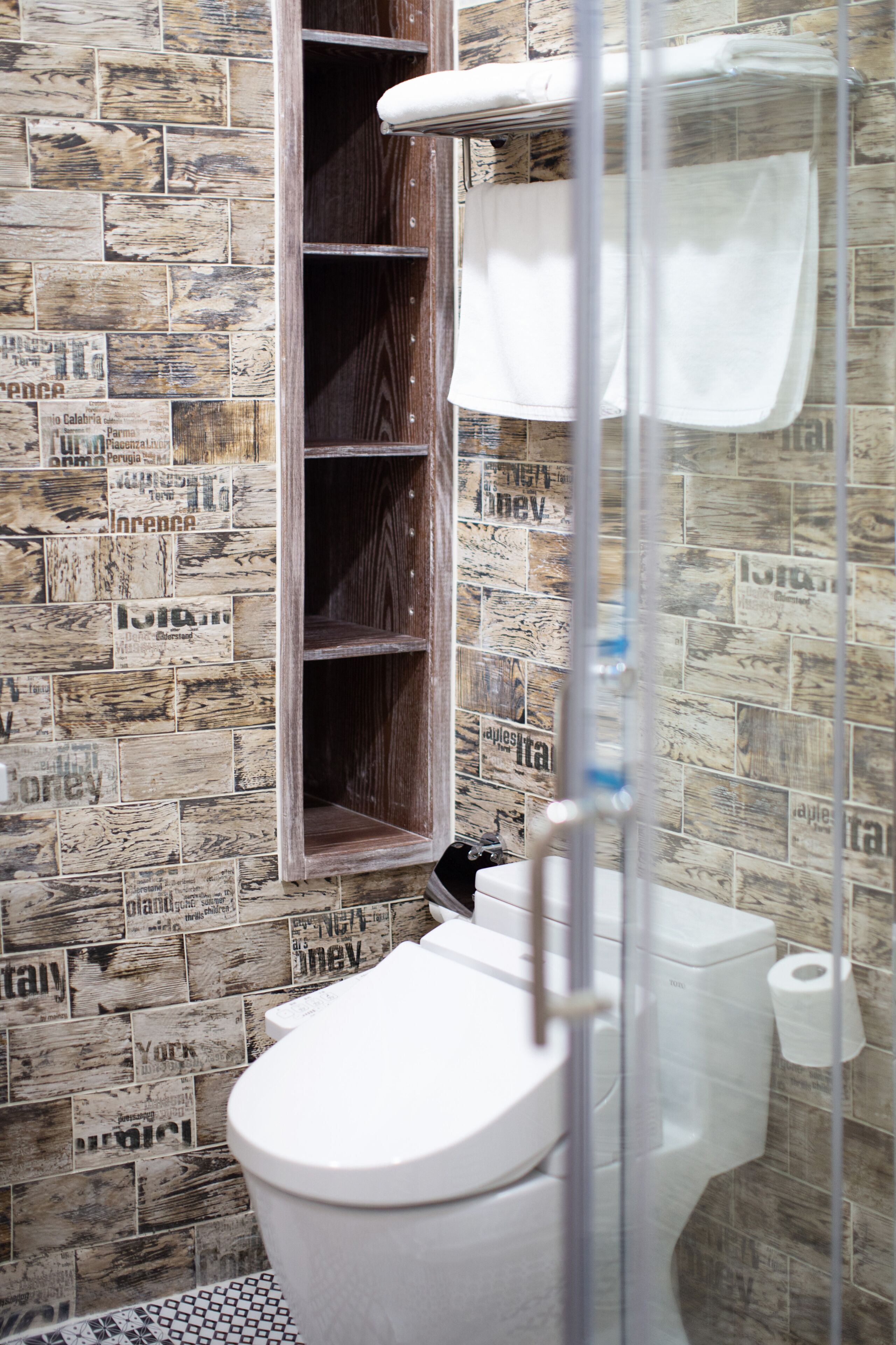 Un baño con inodoro, cabina de ducha y pared de azulejos con recortes de periódico.