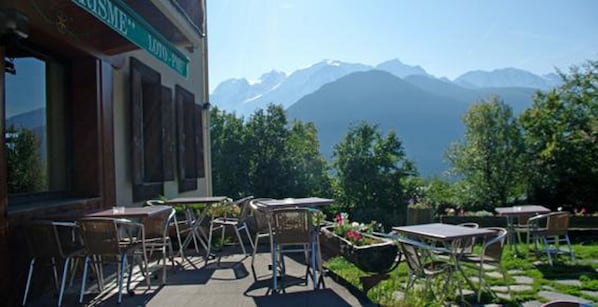 An outdoor seating area with tables and chairs, surrounded by greenery and a mountain view.