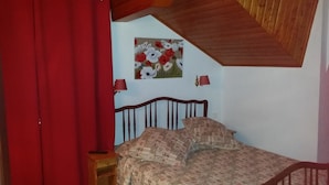 Une chambre à coucher avec une tête de lit en bois, une couvre-lit à motifs, un rideau rouge et un tableau floral accroché au mur.
