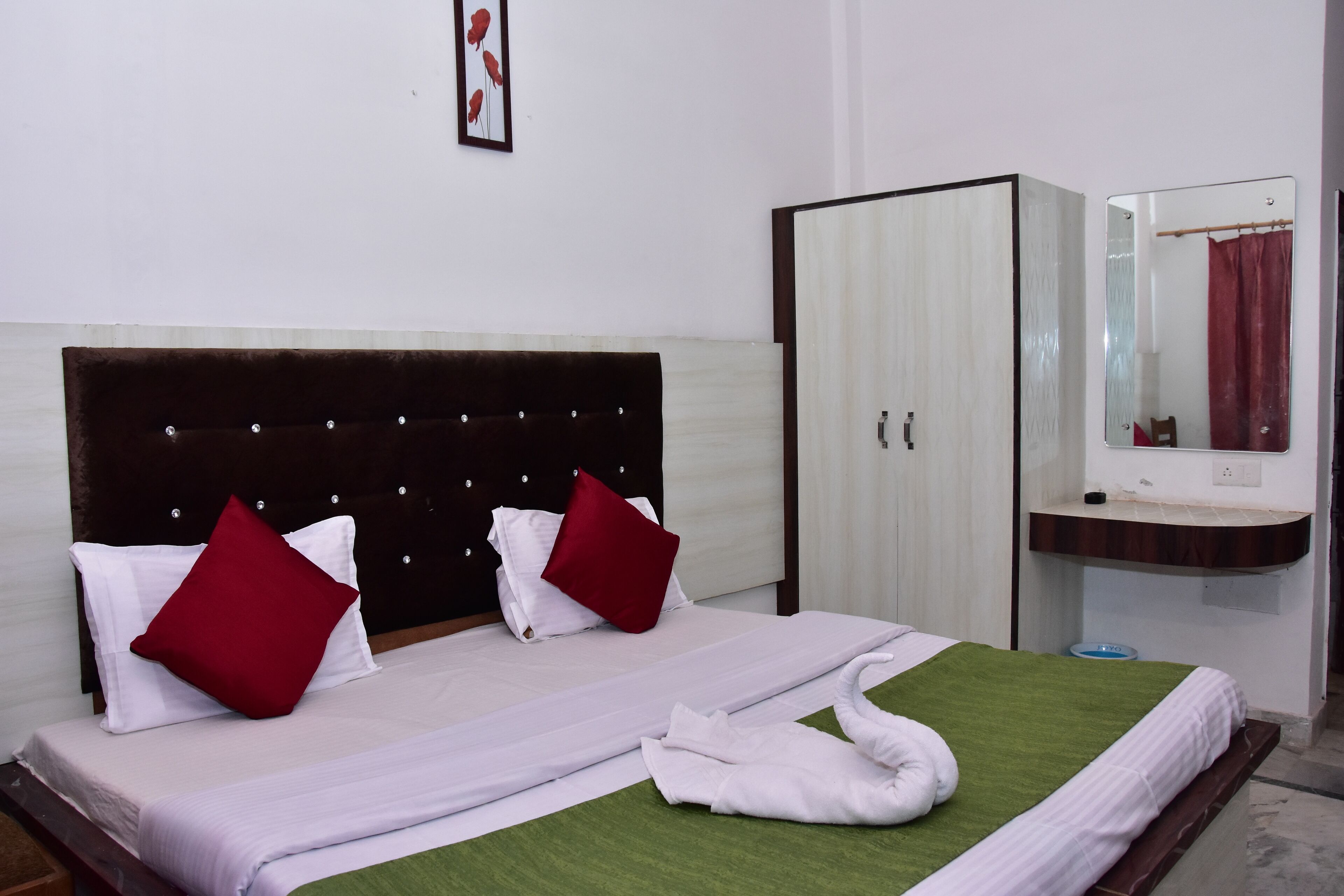 A neatly made bed with white and red pillows, a green bedspread, and a white towel folded on the bed.