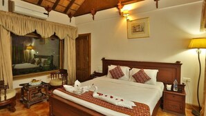 Habitación de hotel elegante con una cama grande, cabecero de madera y vistas a un jardín por la ventana.
