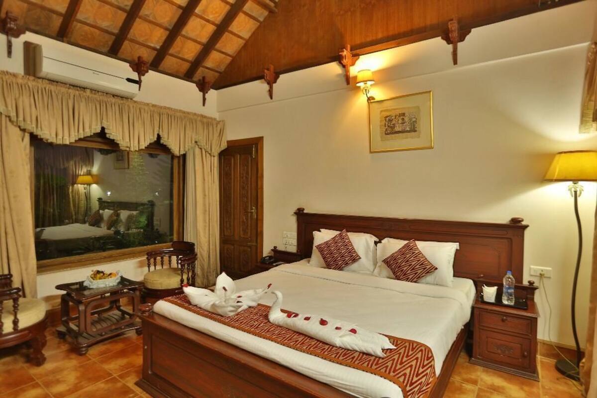 Habitación de hotel elegante con una cama grande, cabecero de madera y vistas a un jardín por la ventana.