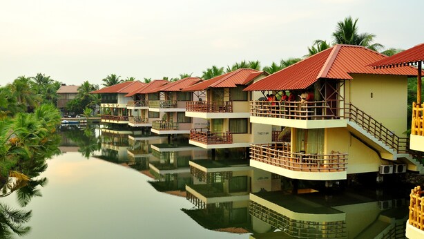 Una hilera de villas flotantes con balcones, conectadas por un canal, rodeadas de palmeras.