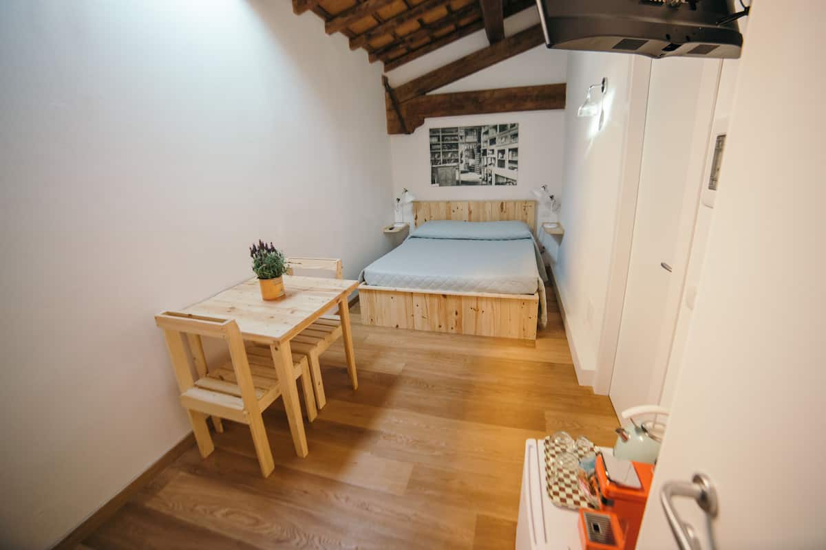 A small bedroom with a wooden bed, a bedside table, a chair, and a small table with a plant.
