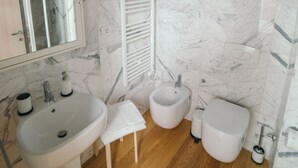 A bathroom with a marble wall, a wooden floor, a sink, a bidet, and a toilet. - Garage Bonci B&B (Pietrasanta)