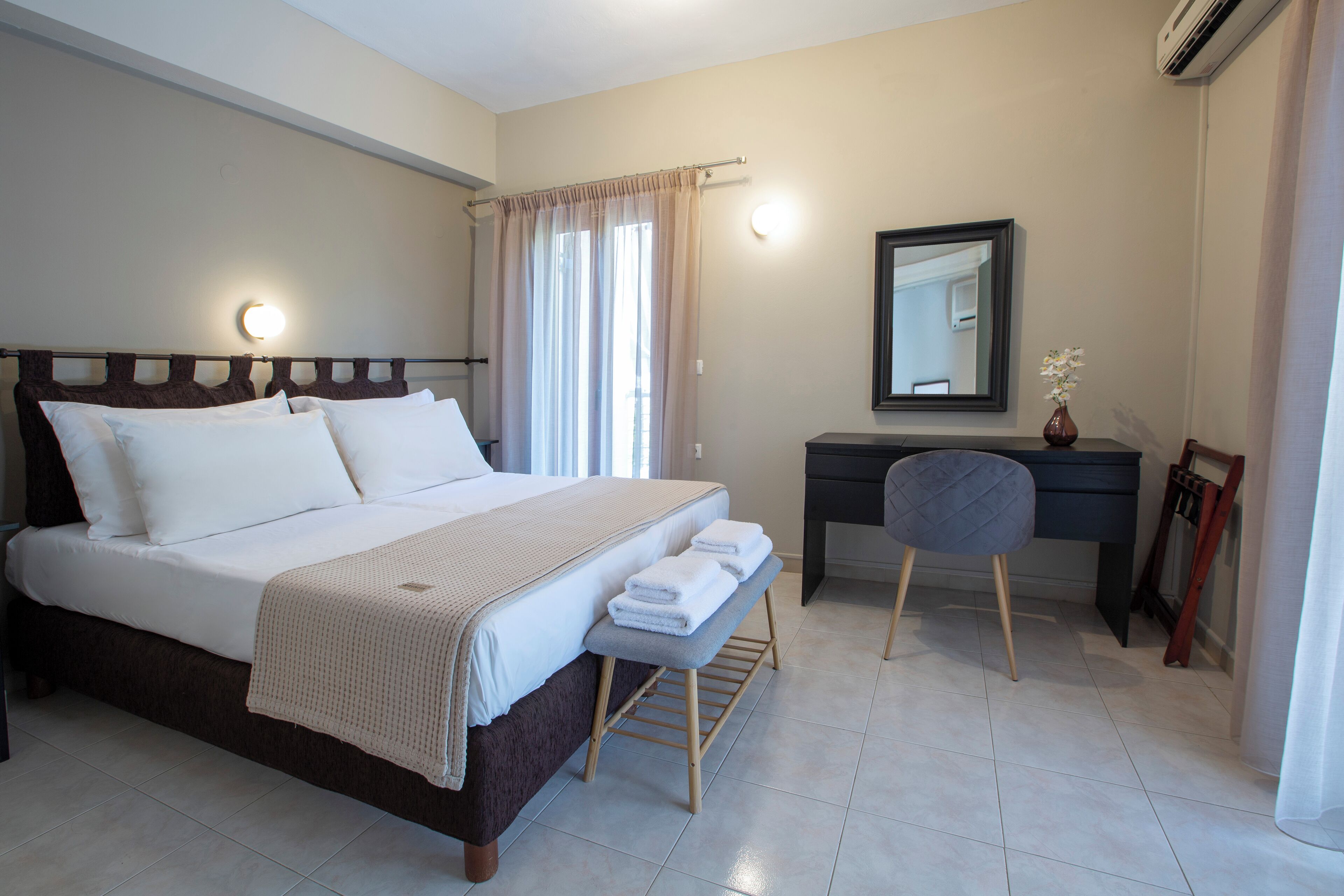 A hotel room with a bed, bedside table, desk, chair, and a mirror.