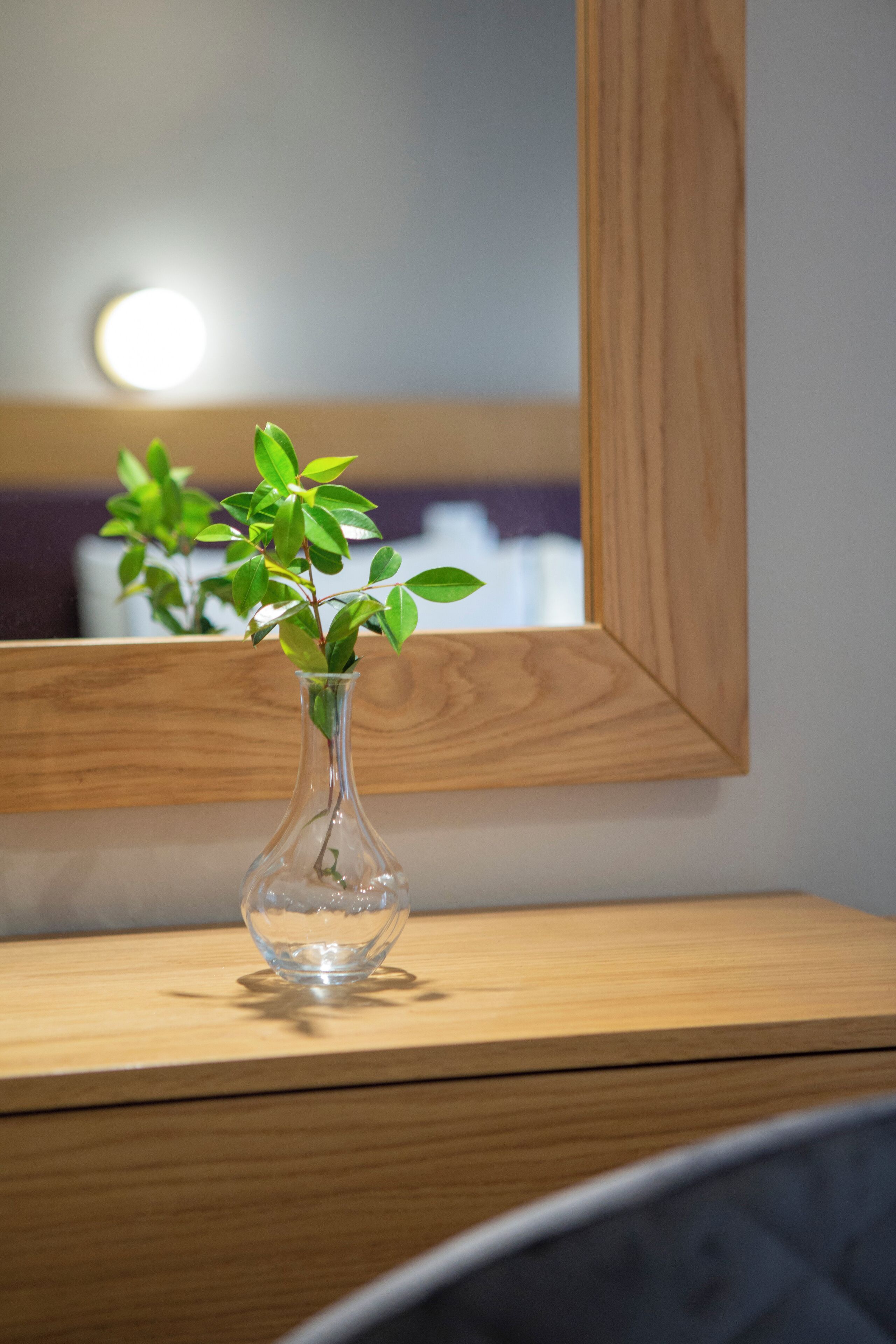 A clear glass vase with green leaves on a wooden surface.