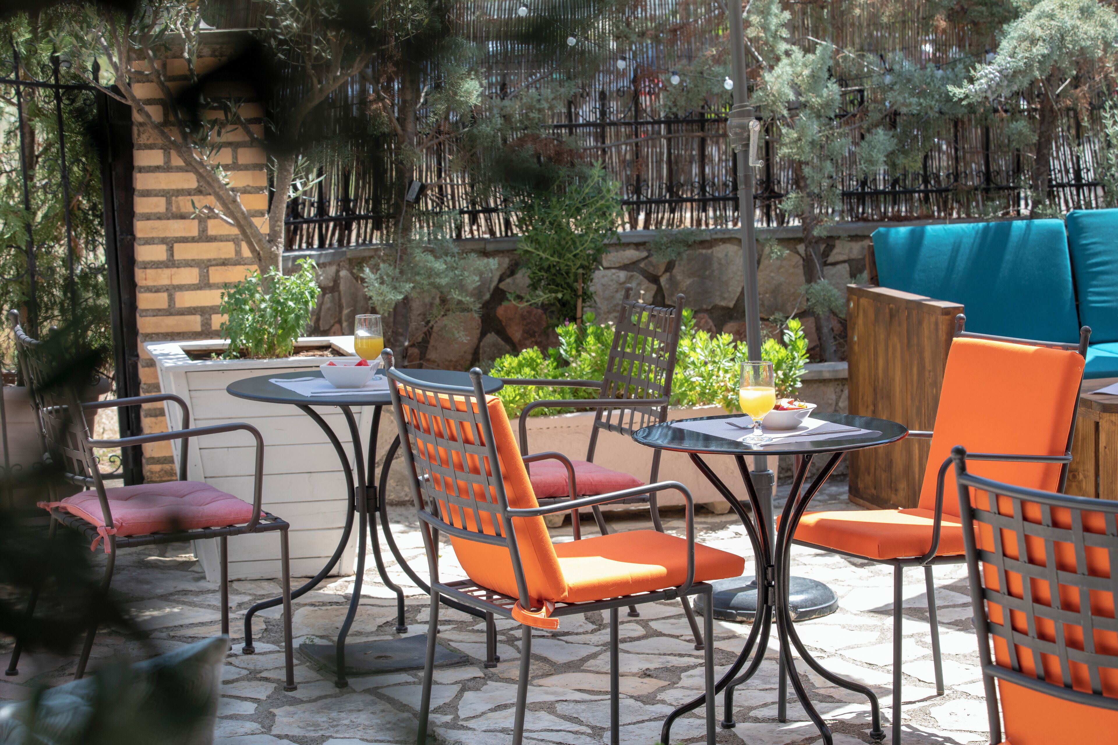 Une terrasse extérieure avec des chaises et des tables en métal, entourée de plantes et d’un mur en pierre.