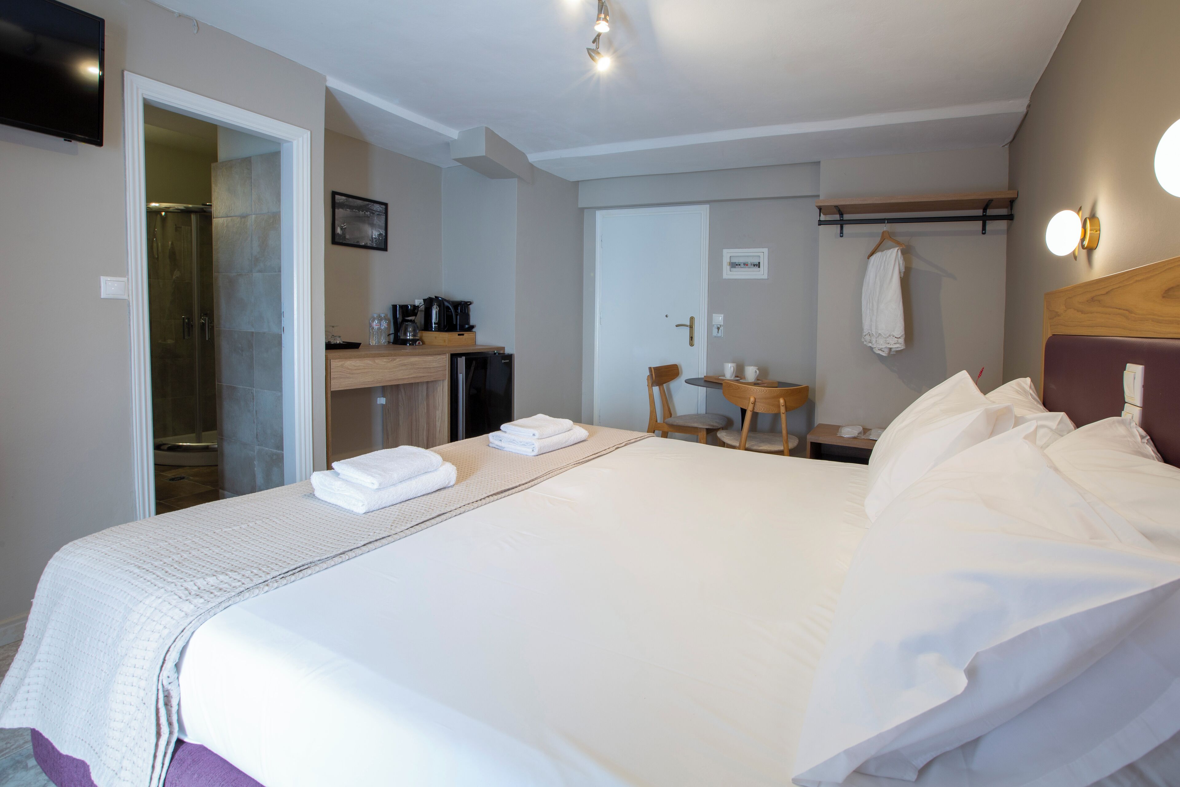 A hotel room with a bed, a desk, a chair, a small table, a shower area, and a television.