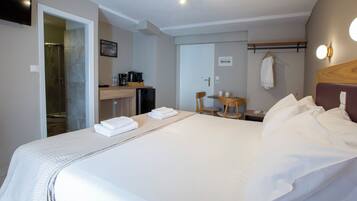 A hotel room with a bed, a desk, a chair, a small table, a shower area, and a television.