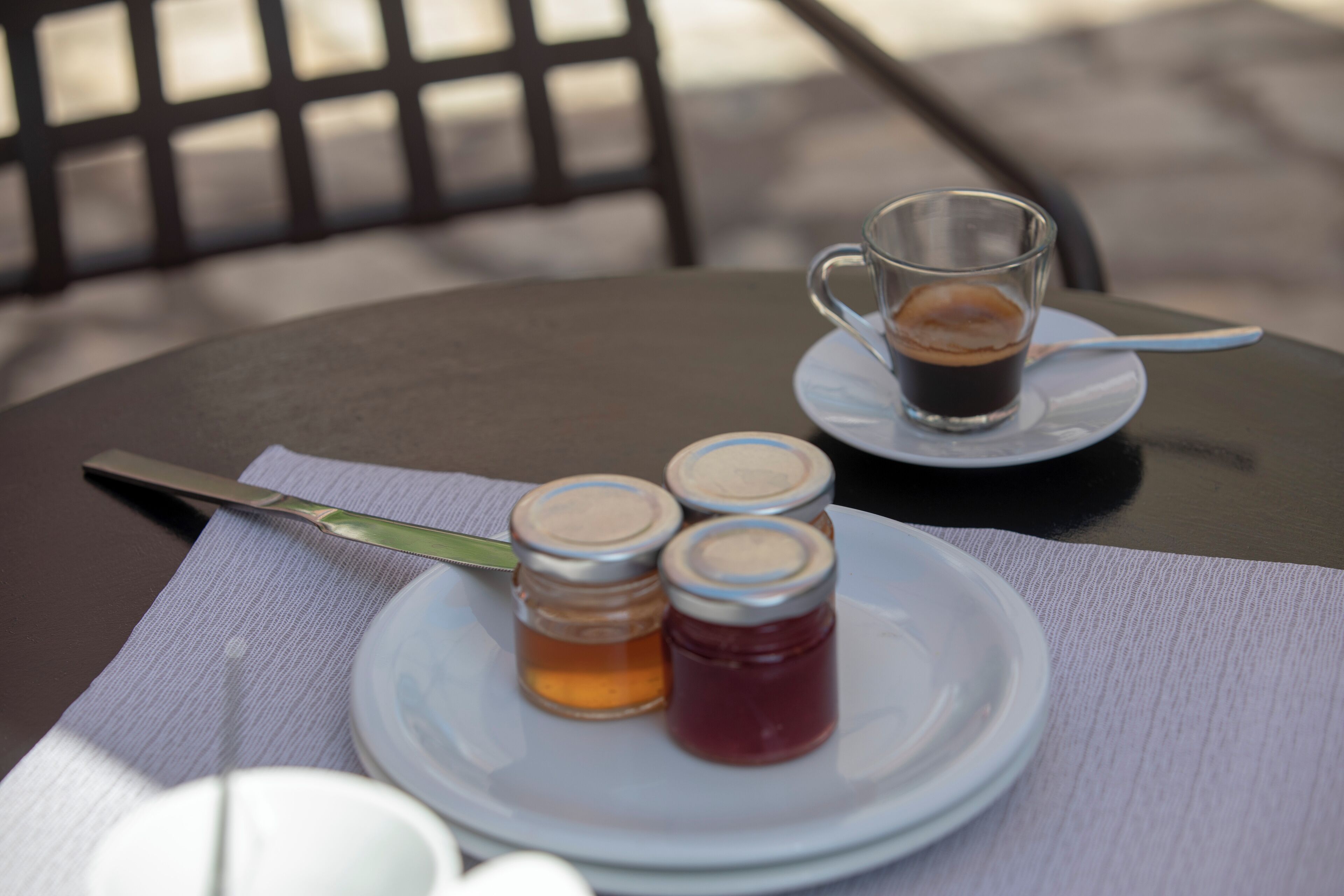 A table with a plate of condiments, a glass of coffee, and a knife on a napkin.