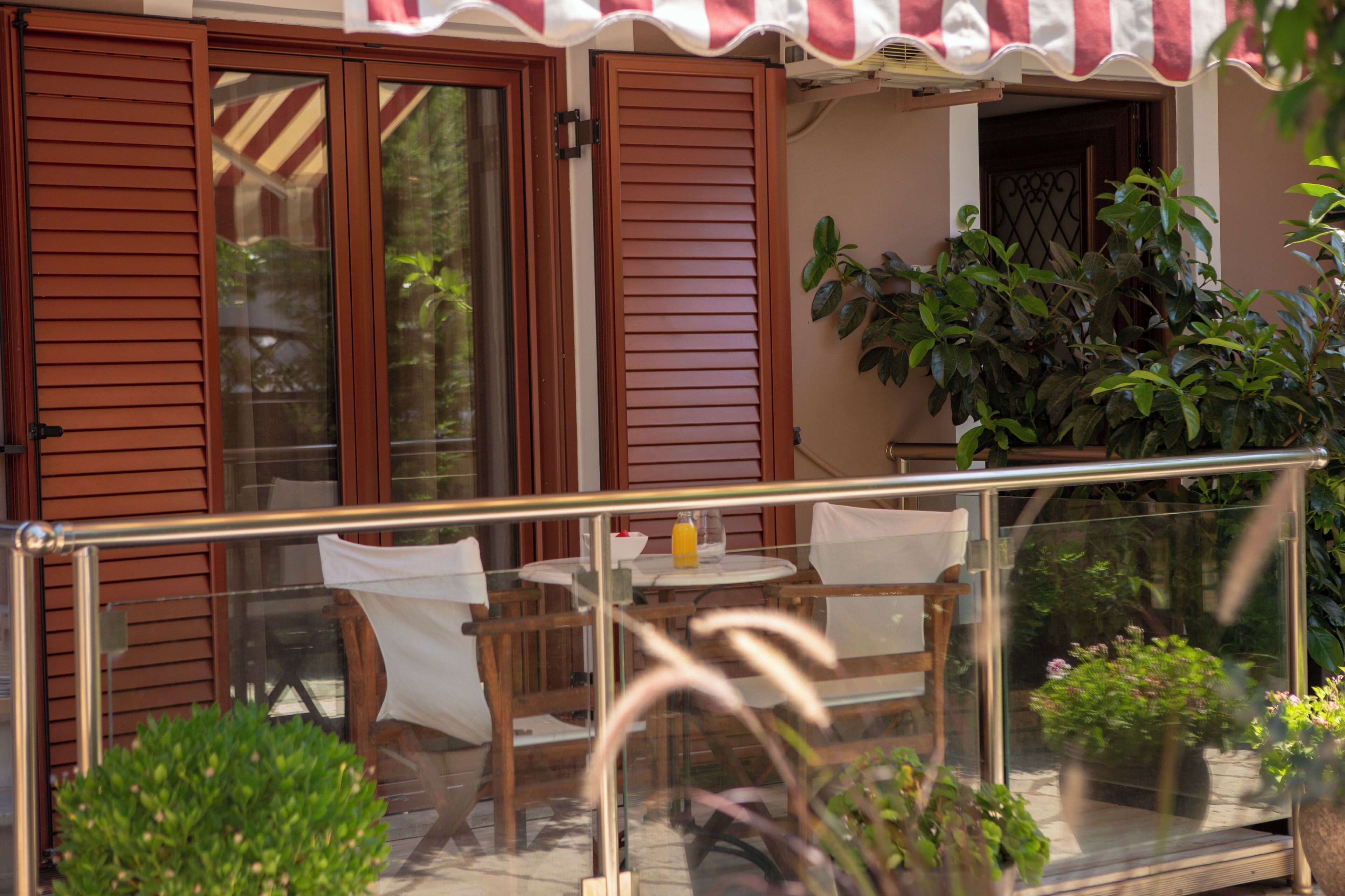 A balcony with a glass railing, wooden chairs, a table, and potted plants.