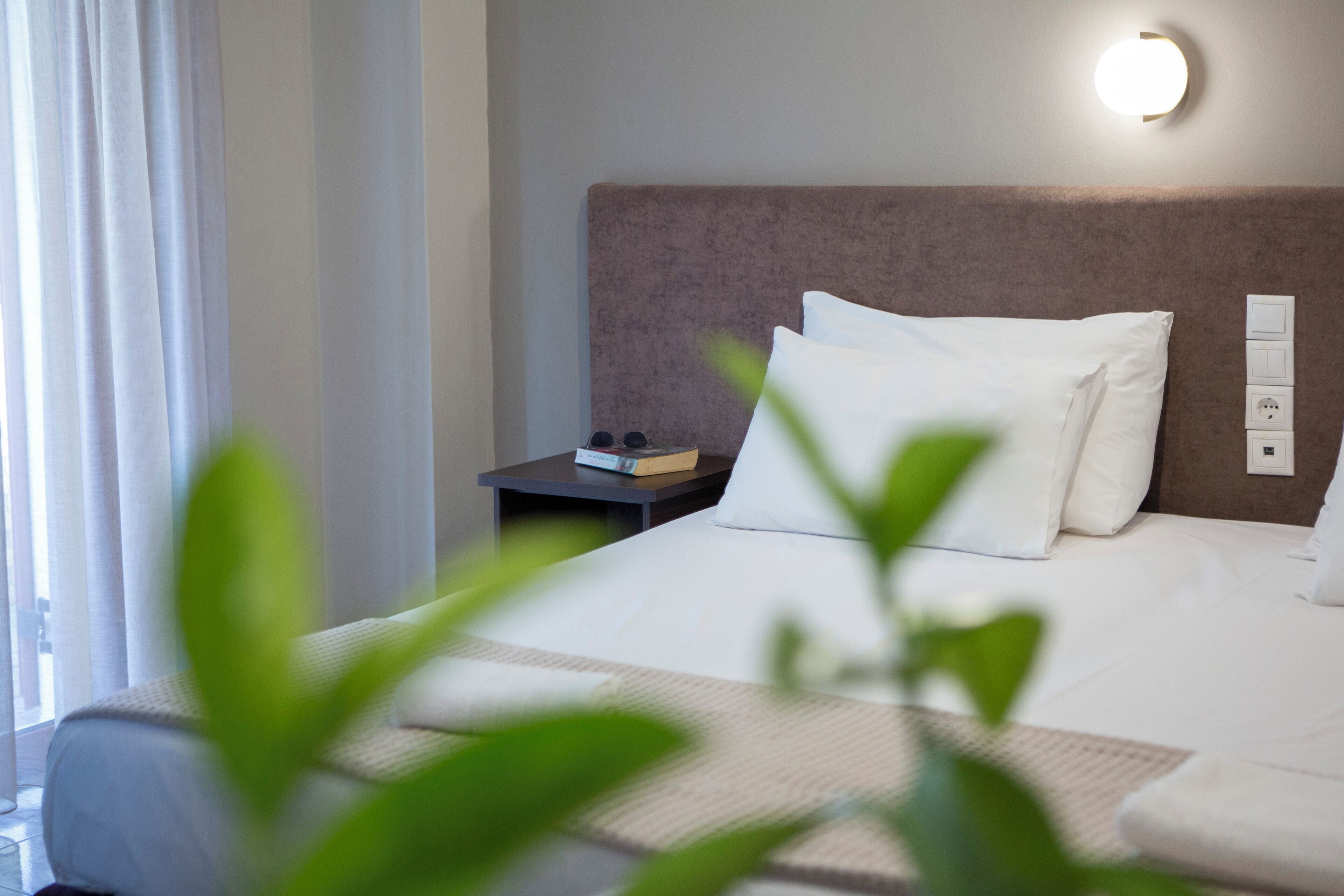 Habitación de hotel con una cama, una mesita de noche, una lámpara de pared y una ventana con cortinas.