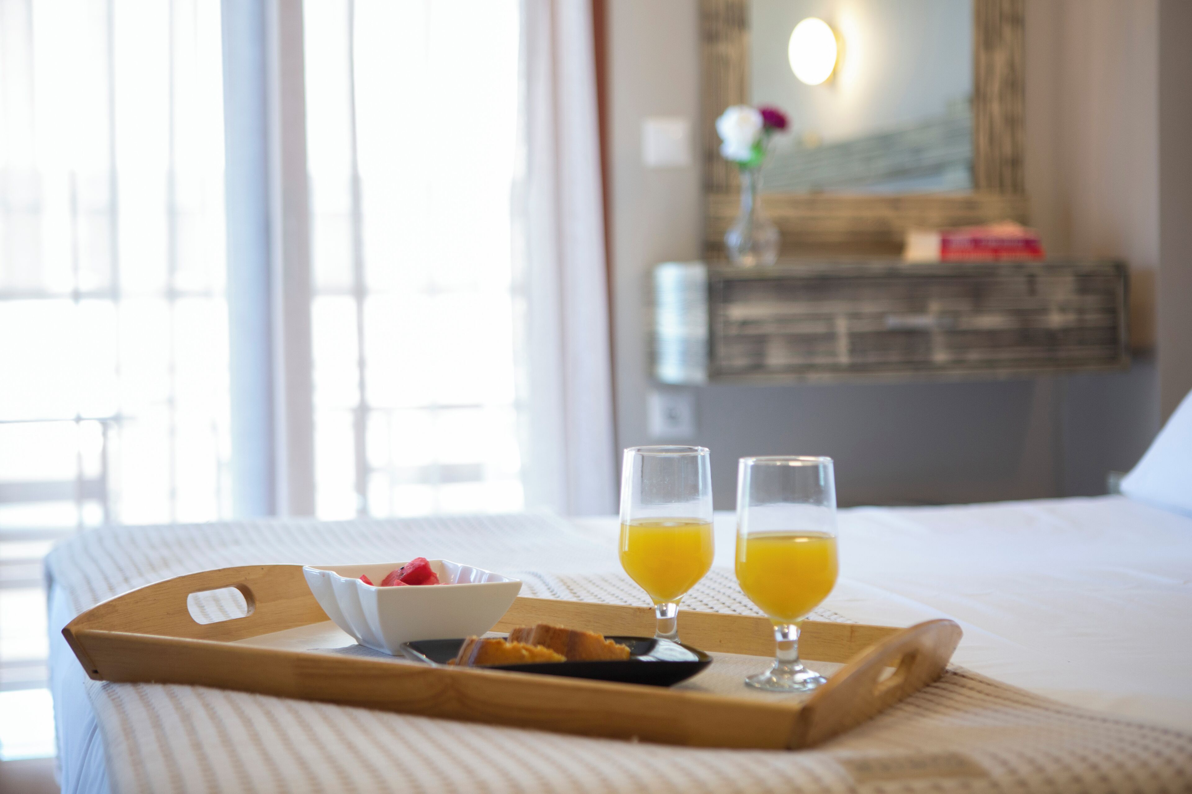 A neatly made breakfast tray with a bowl of fruit, a plate of toast, and two glasses of orange juice on a bed.