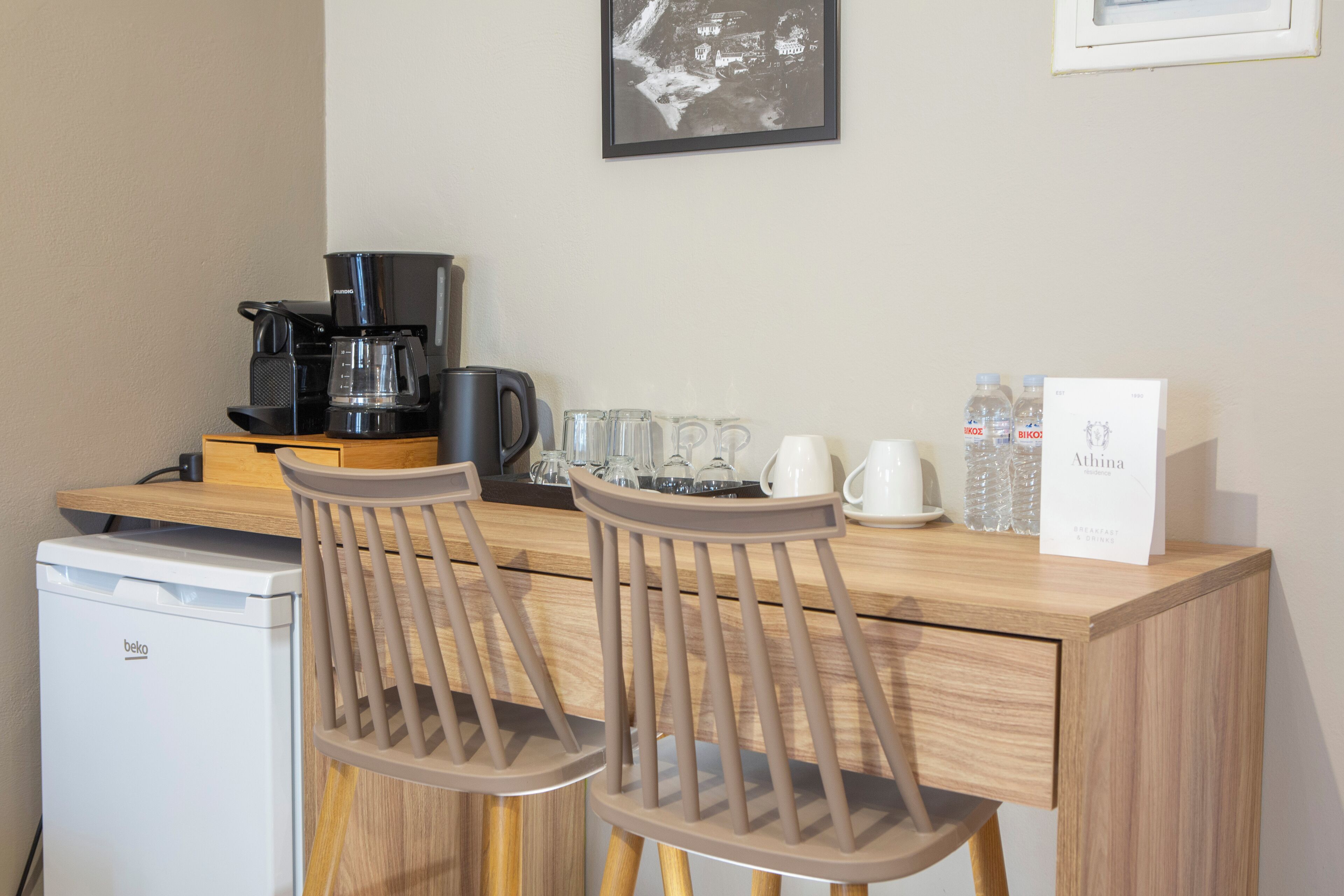 Une petite cuisine équipée d’une machine à café, d’un petit réfrigérateur, de deux tabourets de bar et d’une table basse.