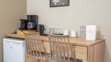 Una kitchenette con cafetera, un refrigerador pequeño, dos taburetes de bar y una mesa de centro.