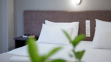 A neatly made bed with white linens and pillows, a bedside table with a book and a small electronic device, and a wall-mounted light fixture.