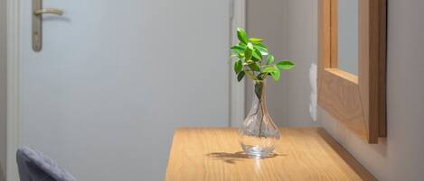 A corner desk with a vase of green plants, a mirror, and a chair.