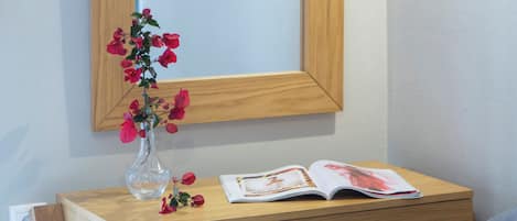 A wooden desk with a mirror, a vase with flowers, and an open magazine.