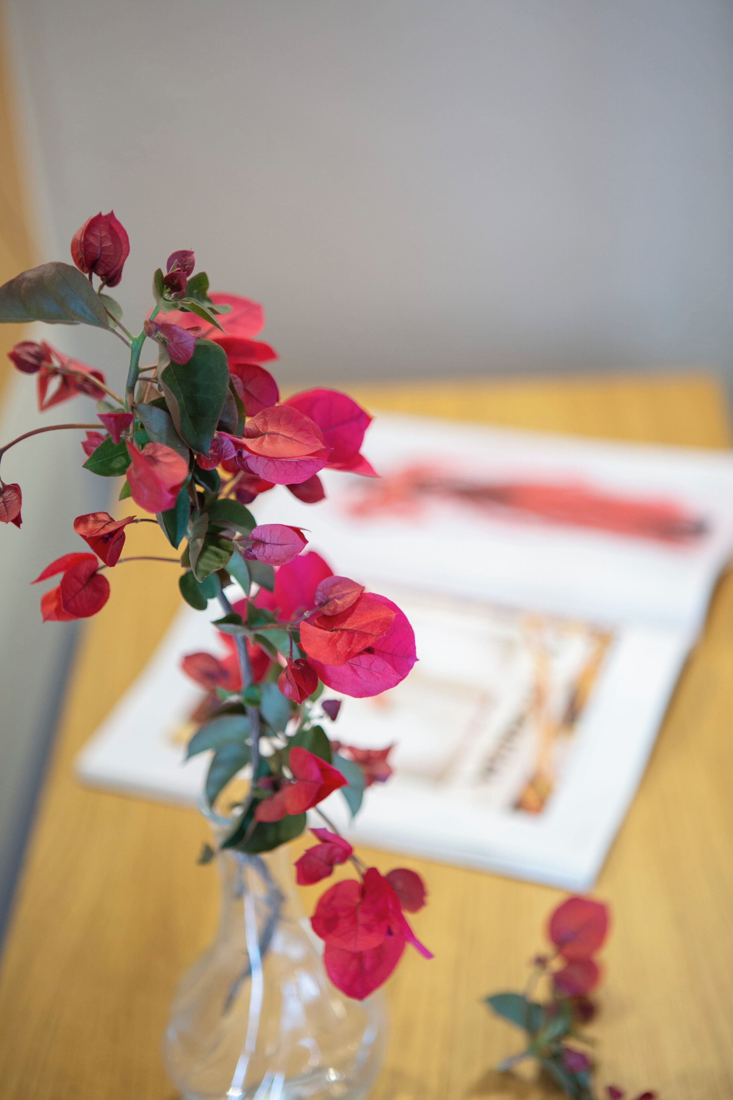 A clear glass vase with pink flowers on a wooden table.