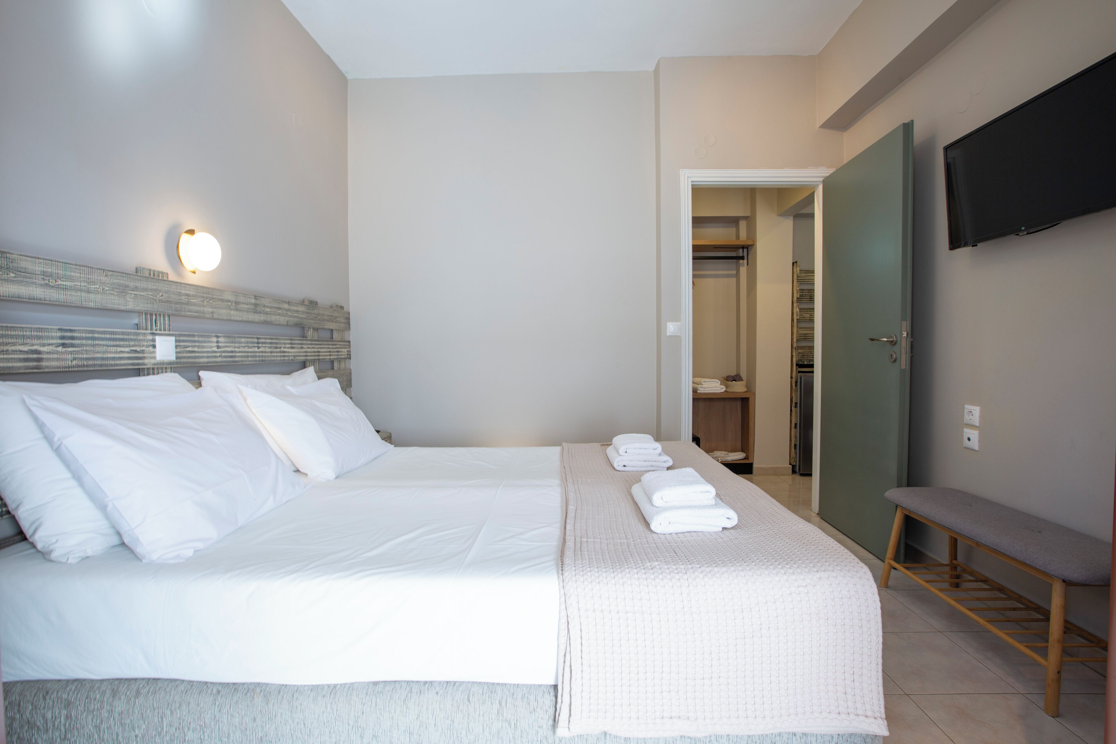 Une chambre d’hôtel avec un grand lit, un banc, une télévision et un dressing.