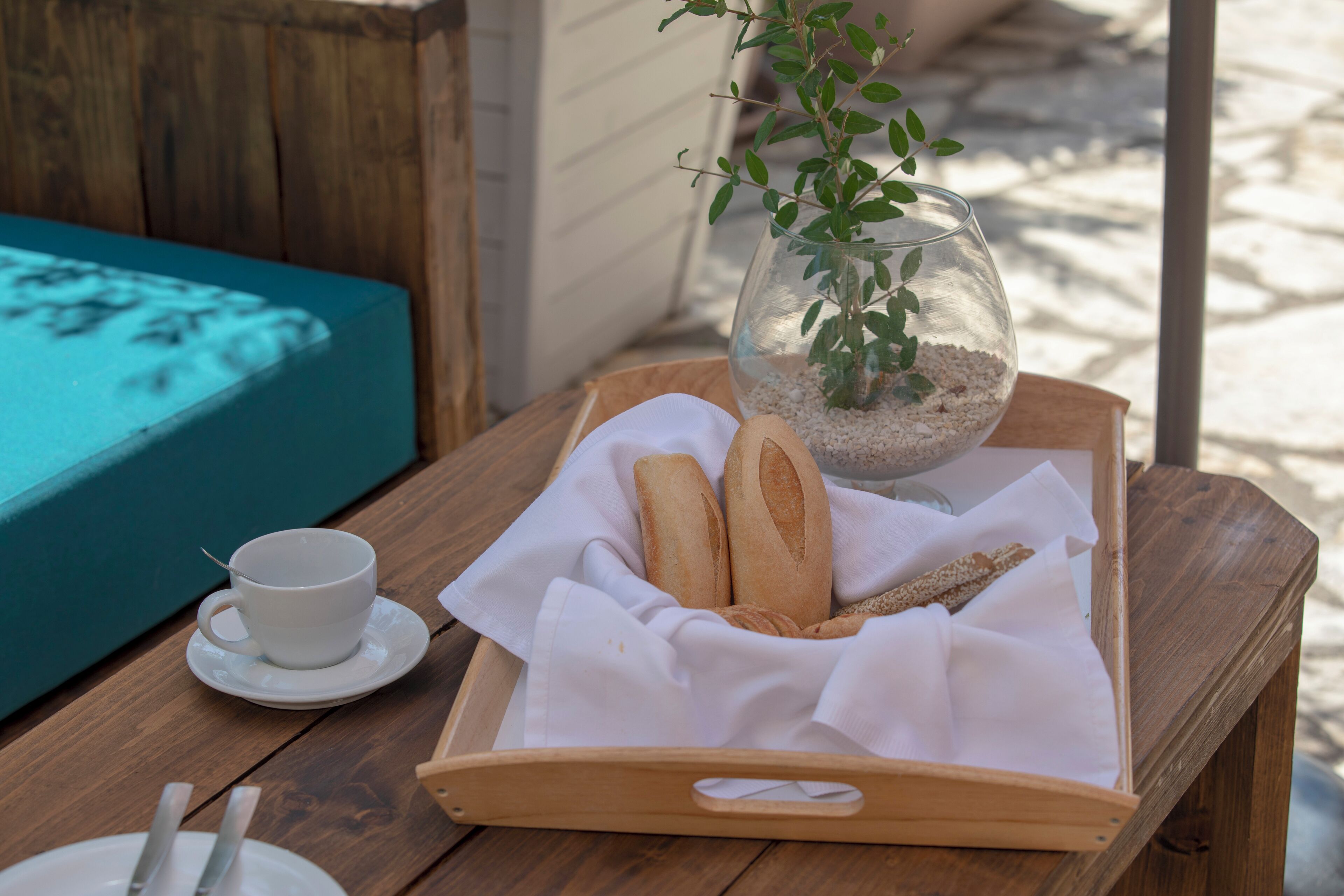 A wooden table with a tray containing bread, a cup, and a glass vase with a plant.