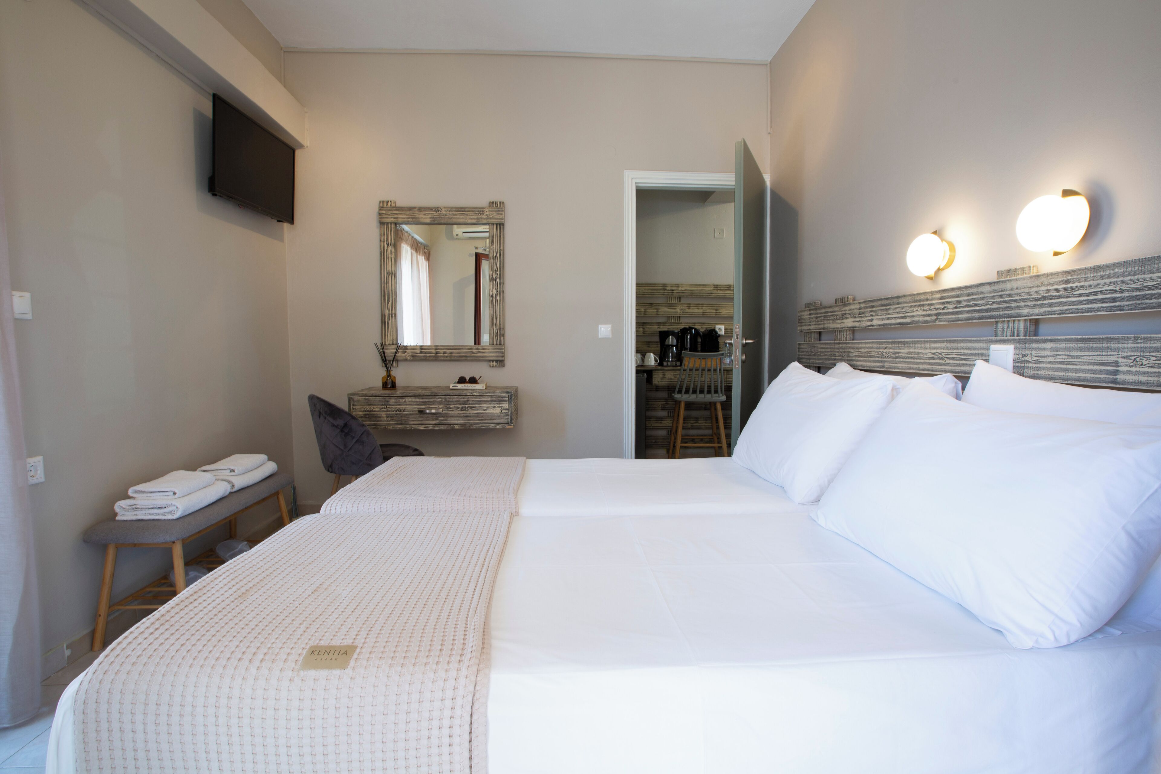 Ein Hotelzimmer mit einem großen Bett, einem an der Wand befestigten Fernseher, einem Spiegel und einer kleinen Sitzecke mit einer Bank und einem Sessel.