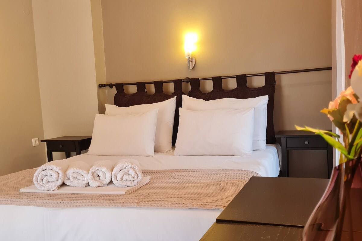 A hotel room with a bed, a nightstand, a vase with flowers, and a wall-mounted light.