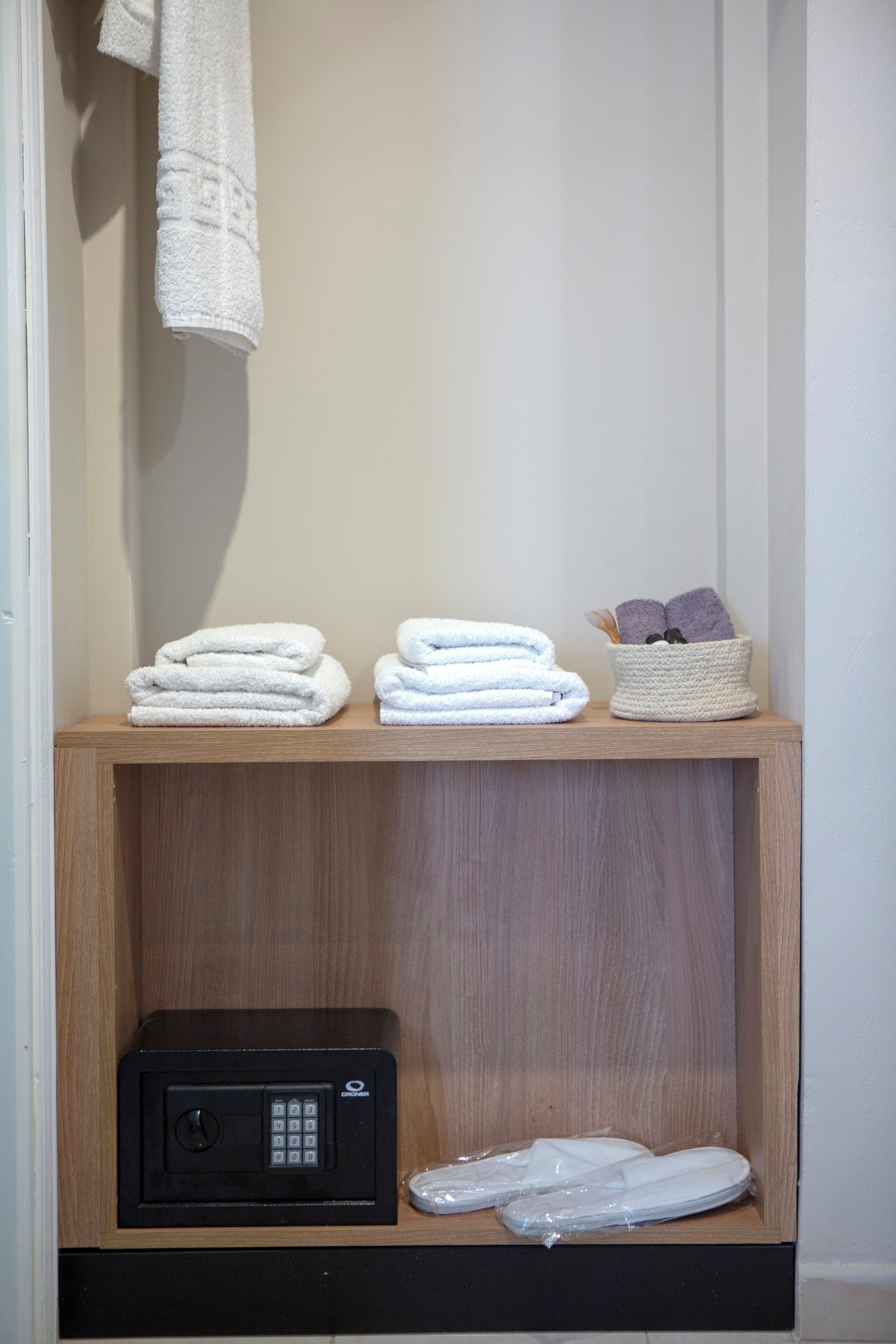 Une étagère en bois avec des serviettes blanches pliées, un petit panier contenant des serviettes violettes et un coffre-fort noir.