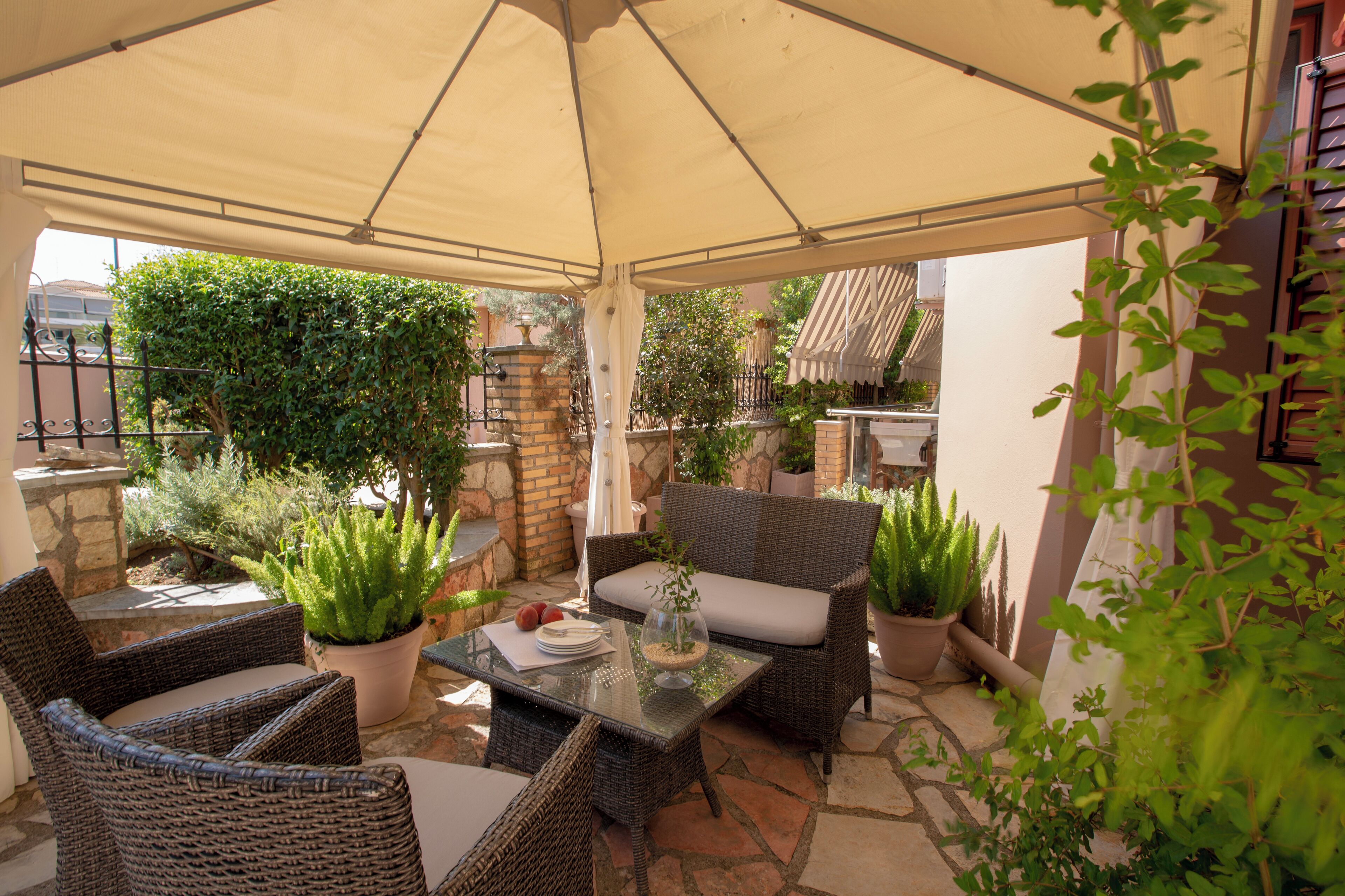 An outdoor patio area with wicker furniture, potted plants, and a table set for dining.