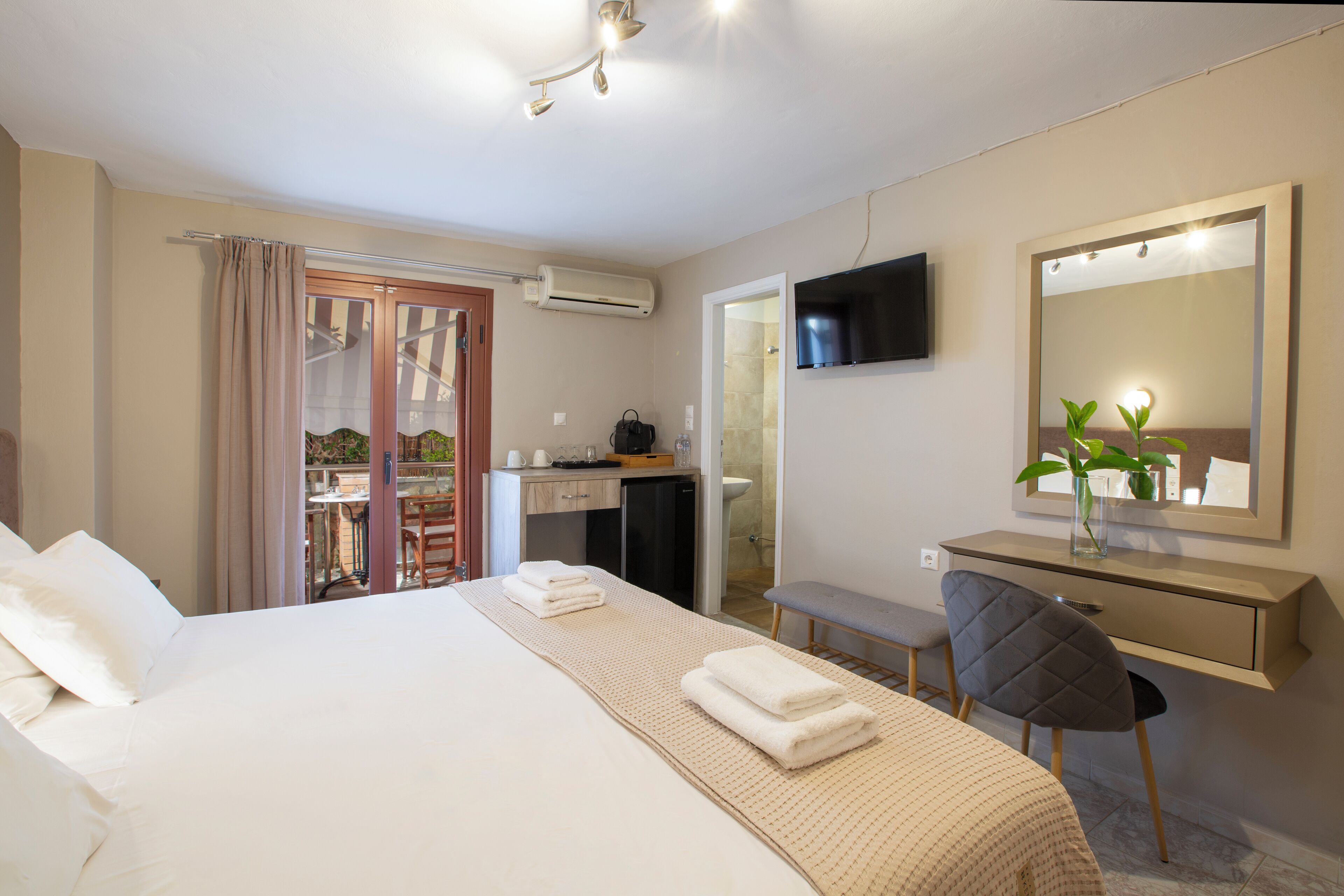 A hotel room with a bed, a desk, a chair, a TV, and a bathroom visible through an open door.