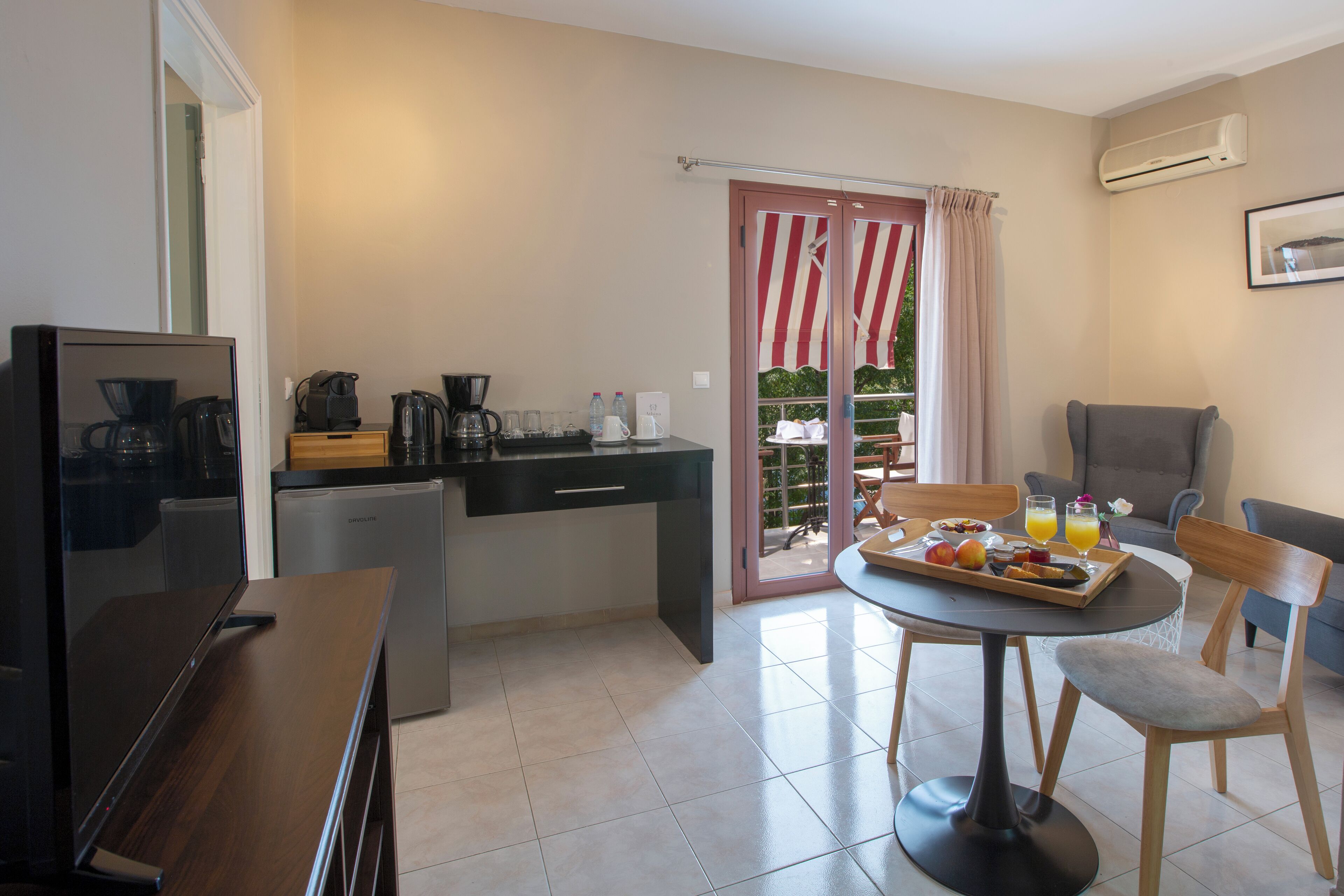 A compact kitchen with a coffee maker, kettle, and toaster, a dining area with a table and chairs, and a sliding glass door leading to a balcony.
