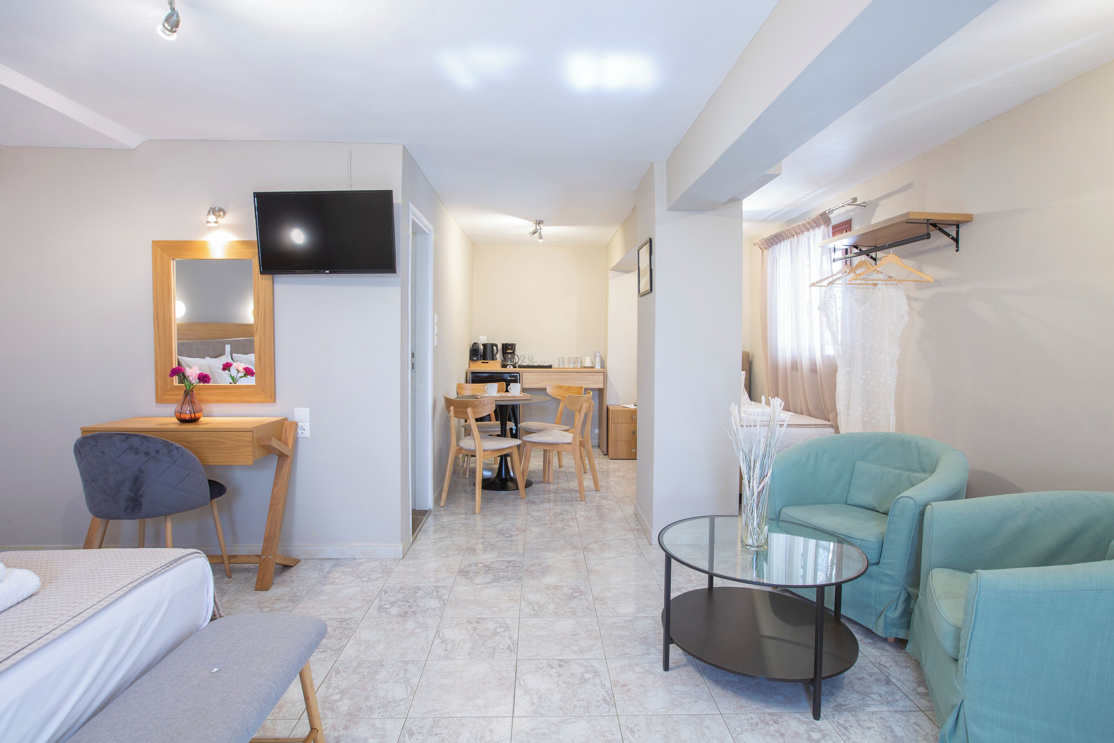 A modern hotel room with a bed, a desk, a chair, a small table, a TV, and a seating area with chairs.