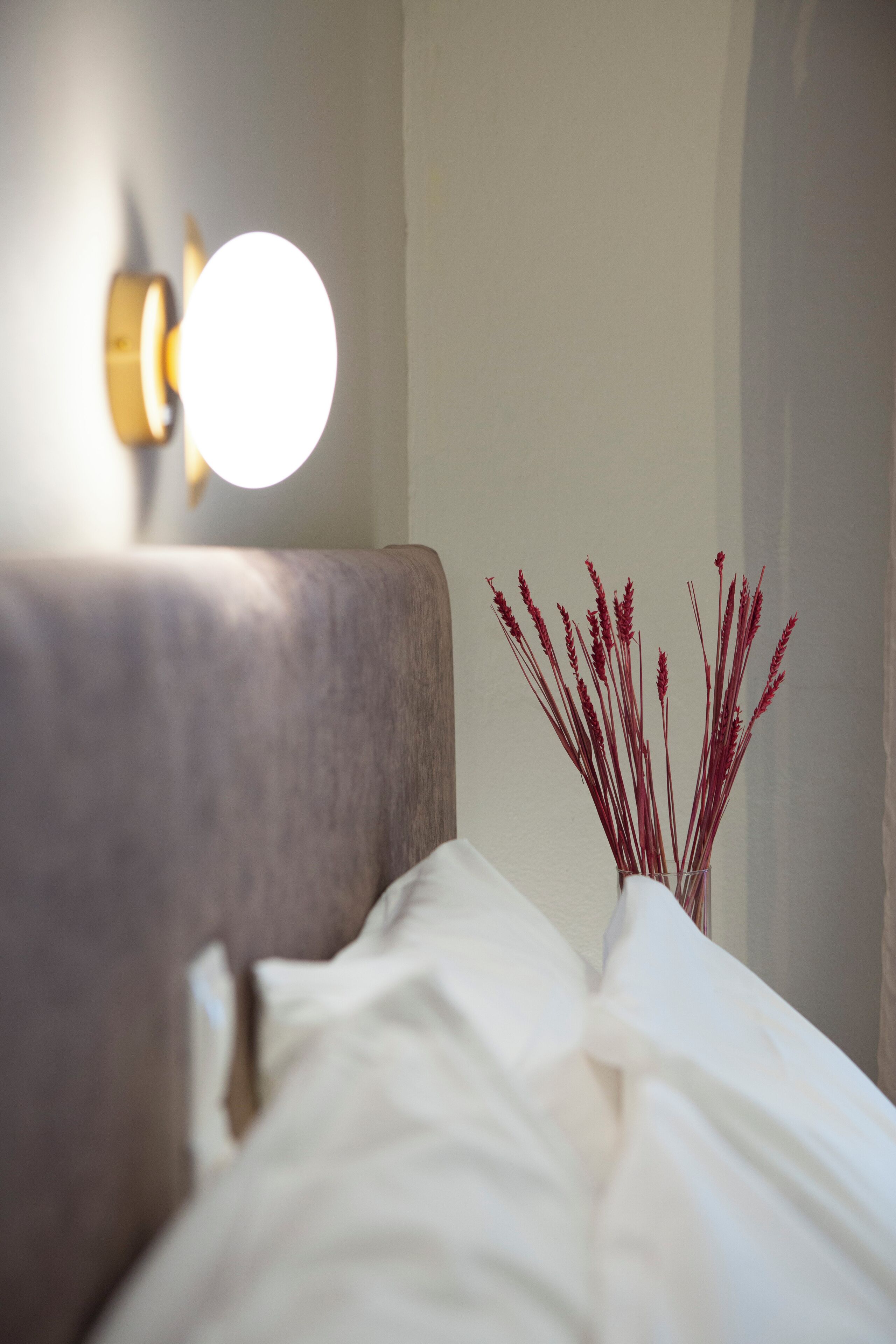 A bed with white bedding and a vase with red flowers on a nightstand.