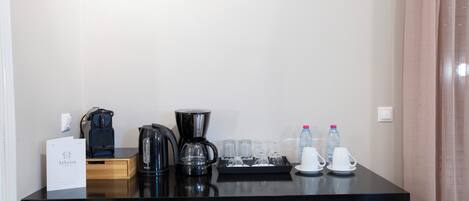 A hotel room's kitchenette with a coffee maker, tea pot, and water bottles.