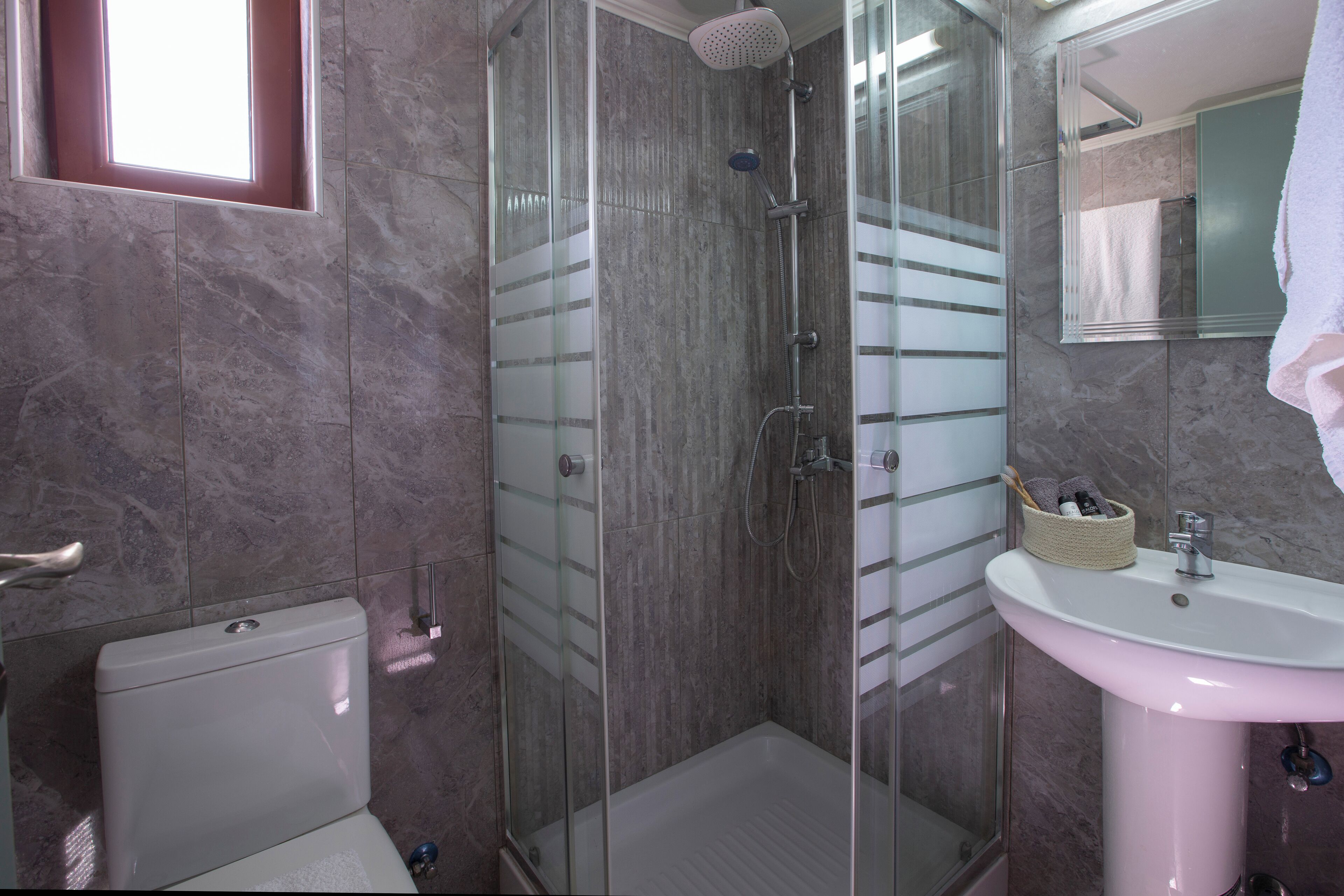 Un baño con ducha envuelta en vidrio, un lavamanos blanco y un inodoro.