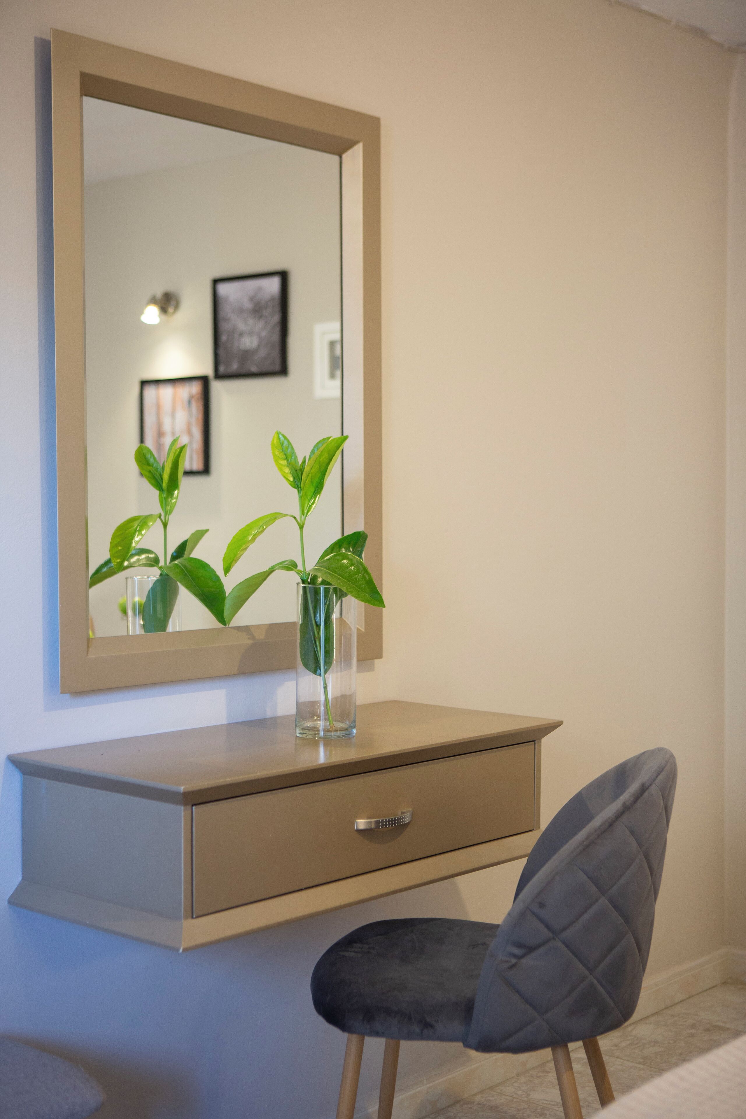 A modern room with a beige dresser, a mirror, a small plant in a clear vase, and a grey upholstered chair.