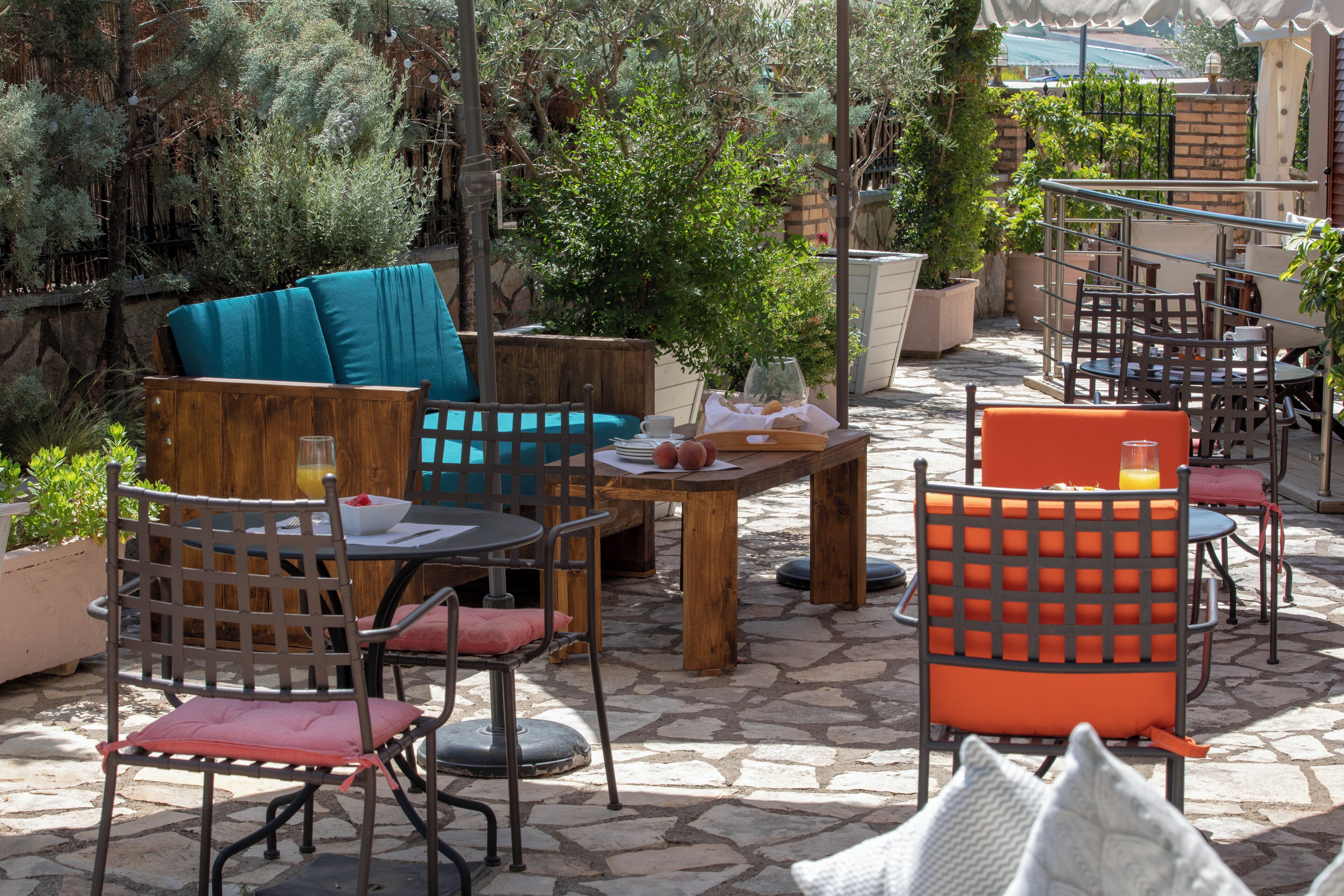 Un espace extérieur aménagé en terrasse, avec des meubles en bois, notamment des chaises et une table, entouré de plantes en pot et doté d’un sol en pierre.