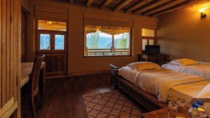 Habitación con piso de madera, dos camas, un escritorio y ventana con vistas a las montañas.
