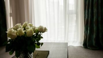A vase with white roses on a table near a window with sheer curtains.