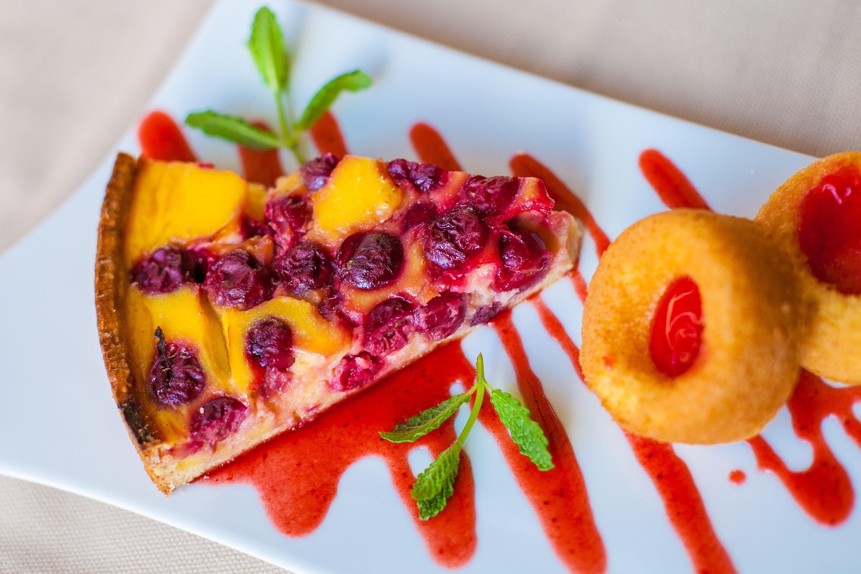 A slice of fruit tart with berries and a drizzle of red sauce, accompanied by two small pastries.