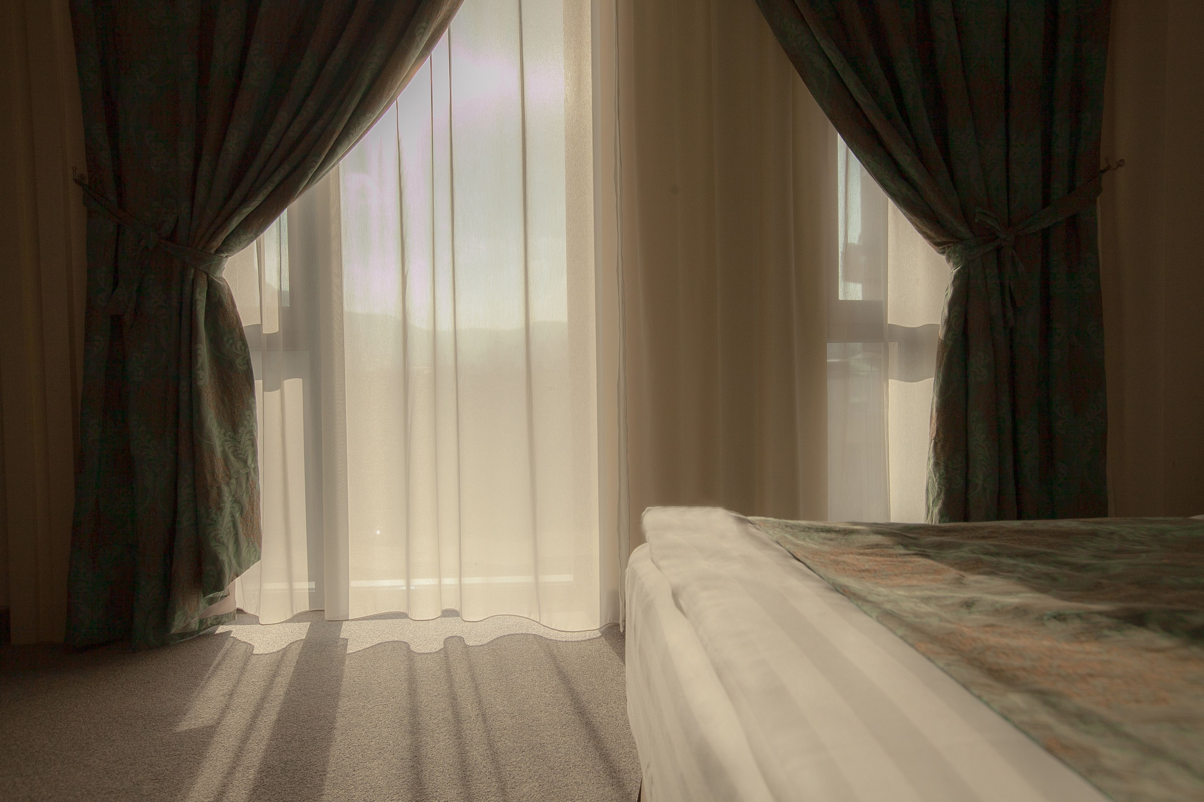 Ein Zimmer mit einem Bett, durchsichtigen Vorhängen und Blick aus dem Fenster.