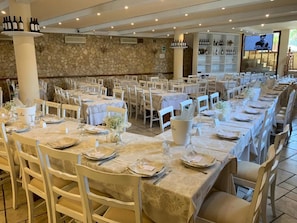 Un restaurante con varias mesas preparadas para comer, una pared de piedra y una exhibición de vinos.