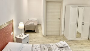 A hotel room with a bed, bedside table with a lamp, a wardrobe, and a door leading to another room. - Romano b&b (Bari)