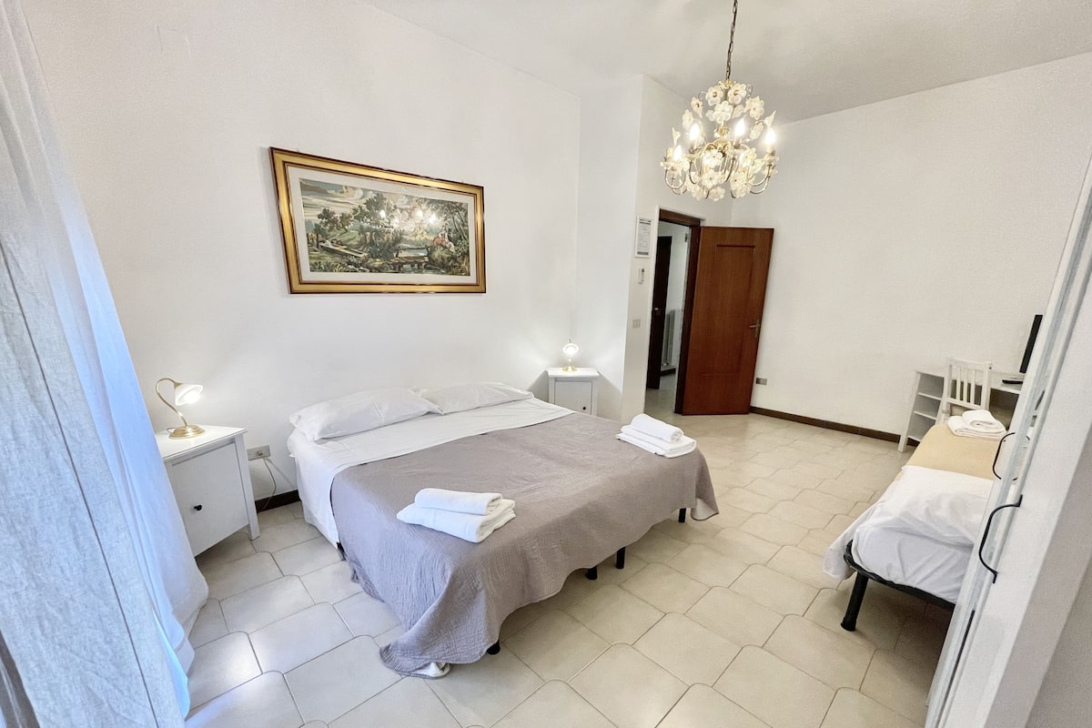 Un dormitorio ordenado con cama, mesitas de noche, un escritorio y una silla.