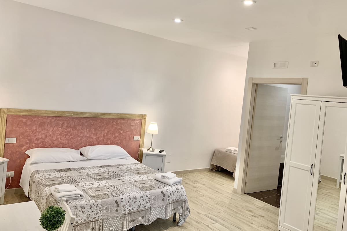 Habitación de hotel con una cama grande, mesitas de noche, lámpara, armario y televisión en la pared.
