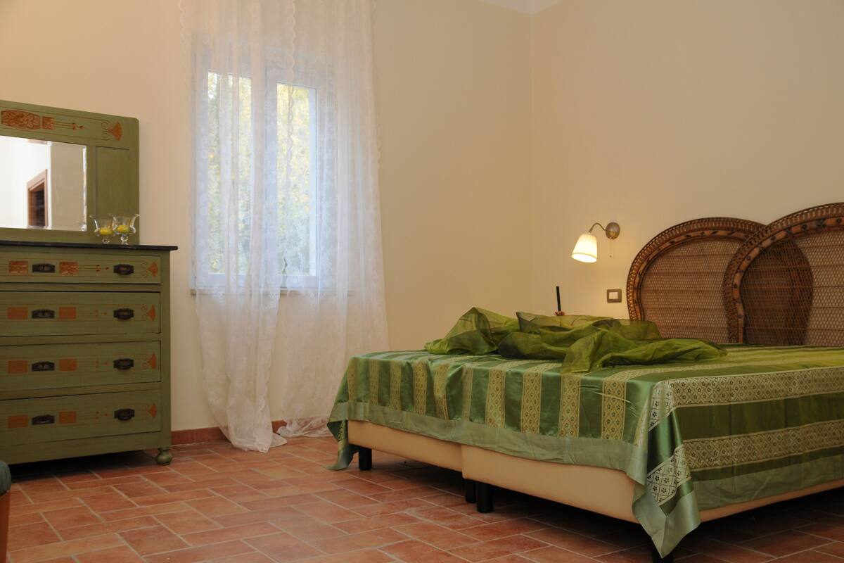 Een slaapkamer met een bed, een dressoir, een spiegel en een raam met gordijnen.