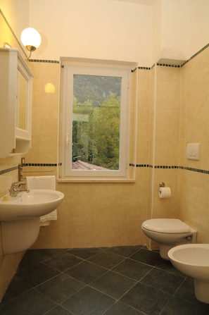 A bathroom with a sink, toilet, and bidet, a window with a view of greenery, and tiled walls. - Oasi La Cascata (Terni)