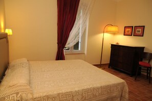 A neatly made bed with a patterned bedspread, a standing floor lamp, a wooden dresser, and two framed pictures on the wall. - Oasi La Cascata (Terni)